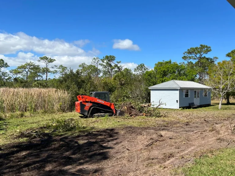 Track loader clearing brush beside a small house