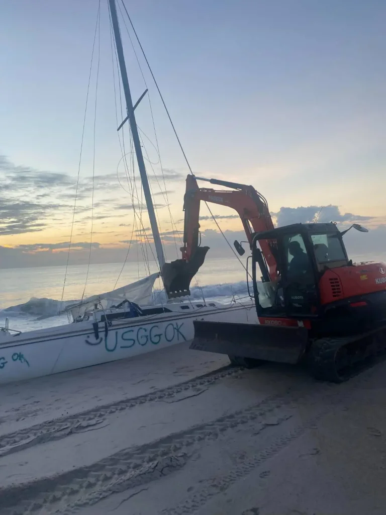 Mini excavator moving a catamaran on the beach at sunset
