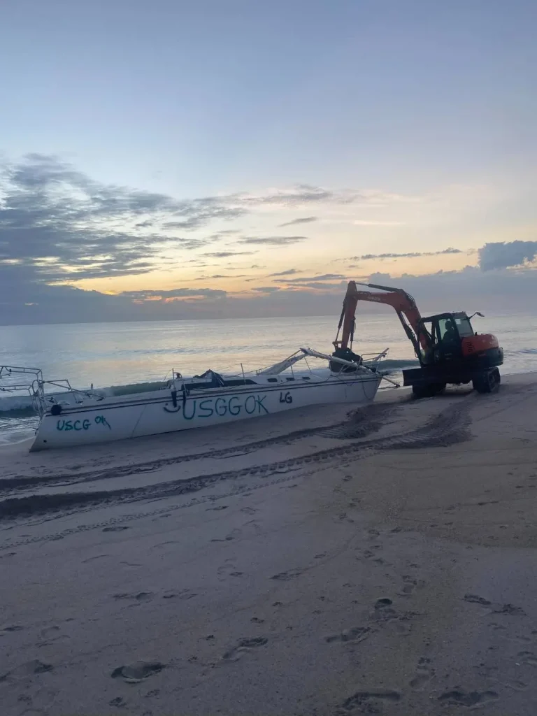 Mini excavator on the beach at dusk beside a boat trailer