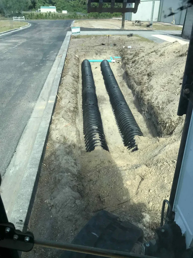 Drainfield pipes in a narrow trench next to a parking lot