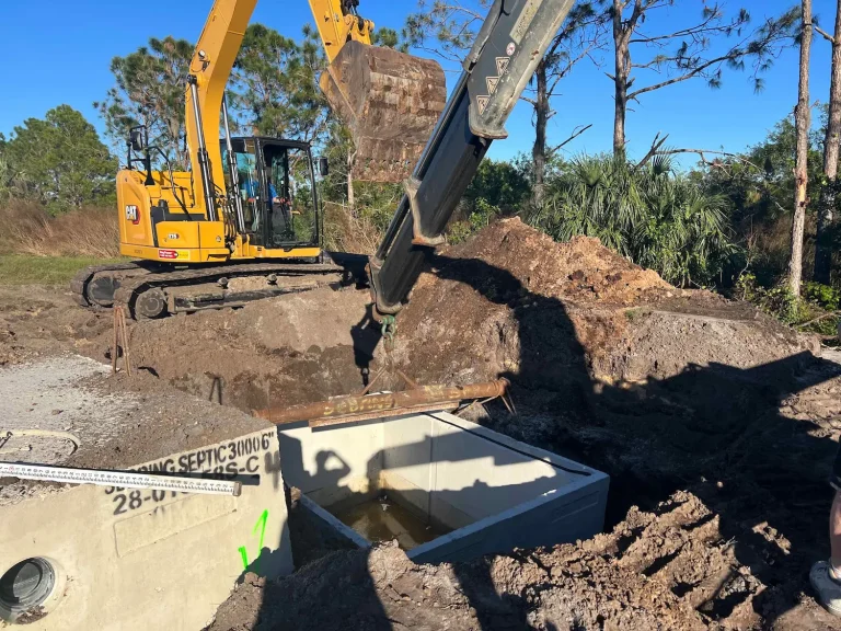 Excavator placing concrete septic tanks on a commercial site