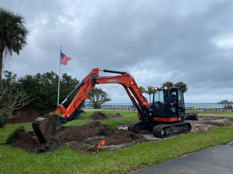 Excavator on a riverfront lawn under a cloudy sky