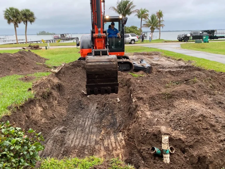 Excavator digging a drainfield trench on a waterfront lawn